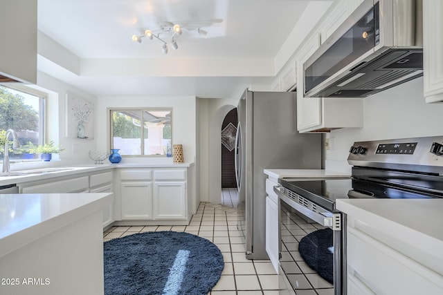 kitchen with sink, light tile patterned floors, a tray ceiling, stainless steel appliances, and white cabinets