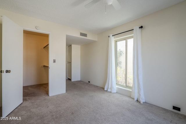 unfurnished bedroom with ceiling fan, a spacious closet, light colored carpet, and a textured ceiling