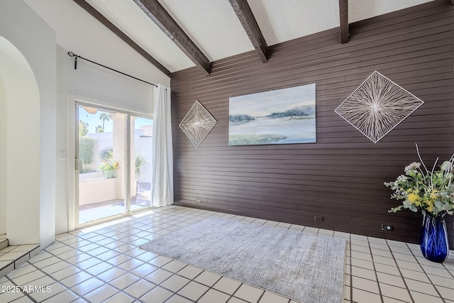 unfurnished room with a textured ceiling, wooden walls, high vaulted ceiling, and beamed ceiling