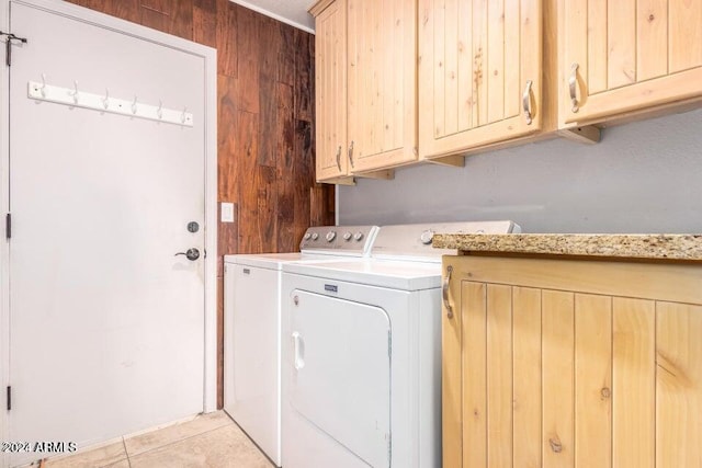 clothes washing area featuring light tile patterned flooring, cabinets, wooden walls, and washing machine and clothes dryer