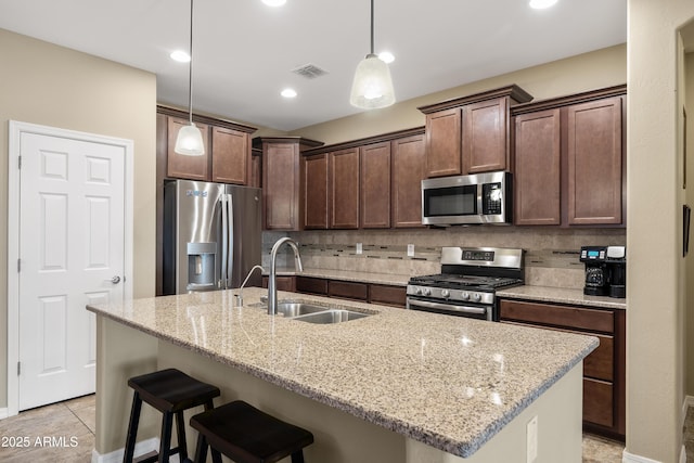 kitchen with light stone counters, a breakfast bar area, stainless steel appliances, decorative backsplash, and a sink