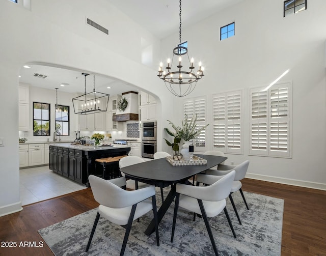 dining room with an inviting chandelier, sink, wood-type flooring, and a high ceiling