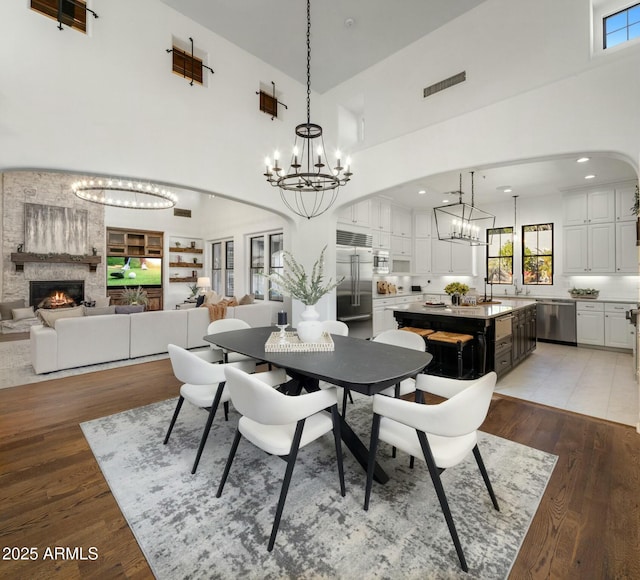 dining space with hardwood / wood-style flooring, a stone fireplace, a chandelier, and a towering ceiling