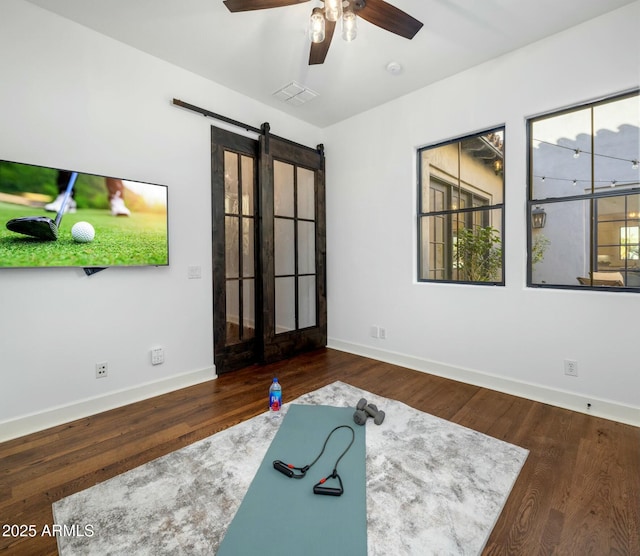 workout room featuring ceiling fan, a barn door, and dark hardwood / wood-style flooring