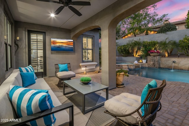 patio terrace at dusk with an outdoor living space, an in ground hot tub, pool water feature, and ceiling fan