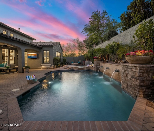 pool at dusk with an in ground hot tub, pool water feature, and a patio area