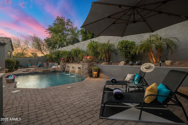 pool at dusk featuring a patio, pool water feature, and an in ground hot tub