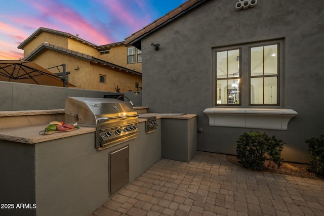 patio terrace at dusk featuring an outdoor kitchen and a grill