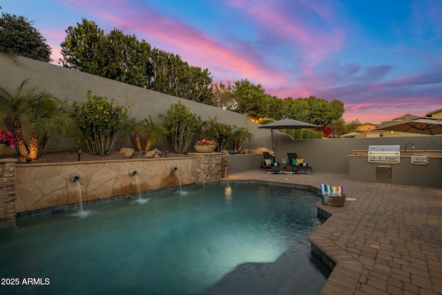 pool at dusk with a patio, an outdoor kitchen, and grilling area