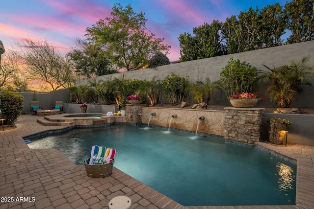 pool at dusk featuring an in ground hot tub and a patio