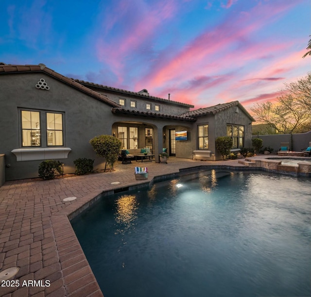 pool at dusk with a patio area and an in ground hot tub