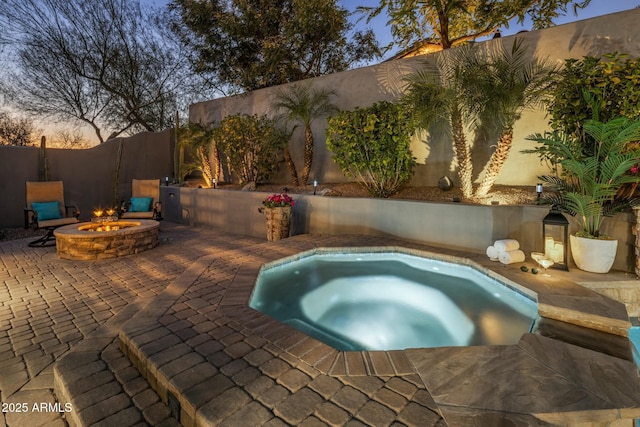 pool at dusk featuring a patio area, an in ground hot tub, and an outdoor fire pit