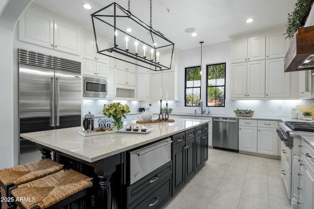 kitchen with sink, white cabinetry, built in appliances, hanging light fixtures, and a kitchen island