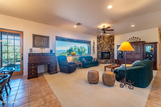 living room with a stone fireplace, ceiling fan, and light tile patterned flooring