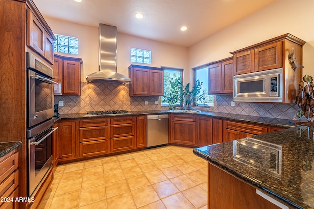 kitchen featuring backsplash, stainless steel appliances, dark stone countertops, and wall chimney range hood