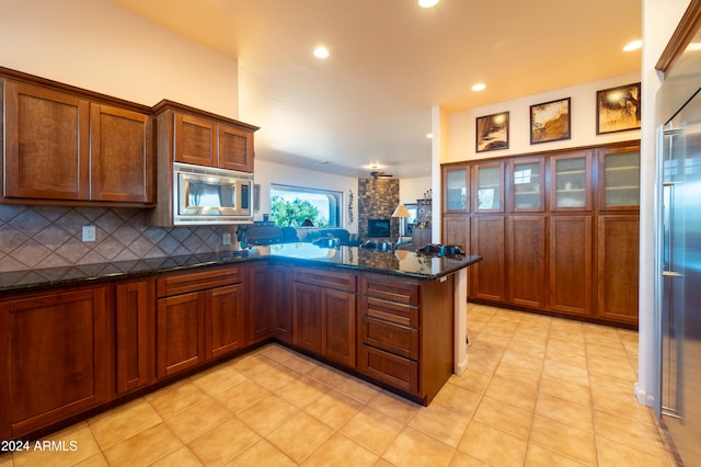 kitchen with kitchen peninsula, built in appliances, dark stone counters, and backsplash