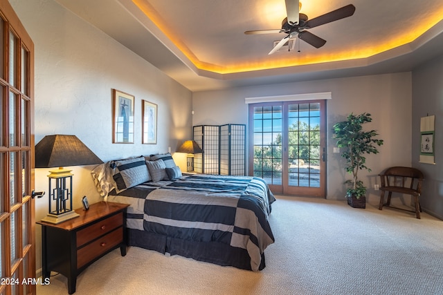 carpeted bedroom with access to exterior, french doors, a tray ceiling, and ceiling fan