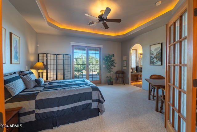 carpeted bedroom with ceiling fan, a raised ceiling, and ensuite bathroom