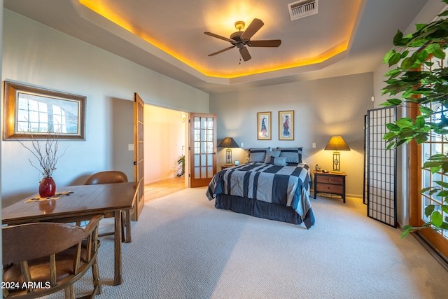 carpeted bedroom featuring a tray ceiling, multiple windows, and ceiling fan