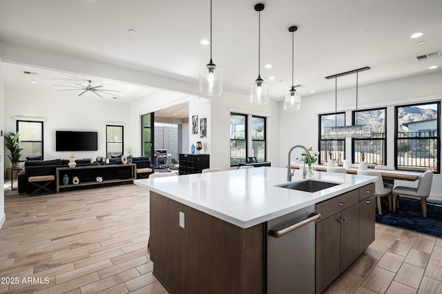 kitchen with dark brown cabinets, sink, pendant lighting, and a kitchen island with sink