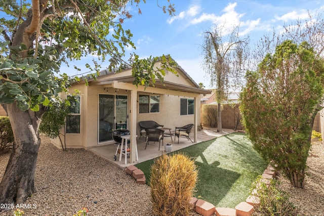 rear view of house with stucco siding, fence, a lawn, and a patio area