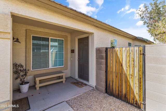 property entrance featuring a gate, fence, and stucco siding