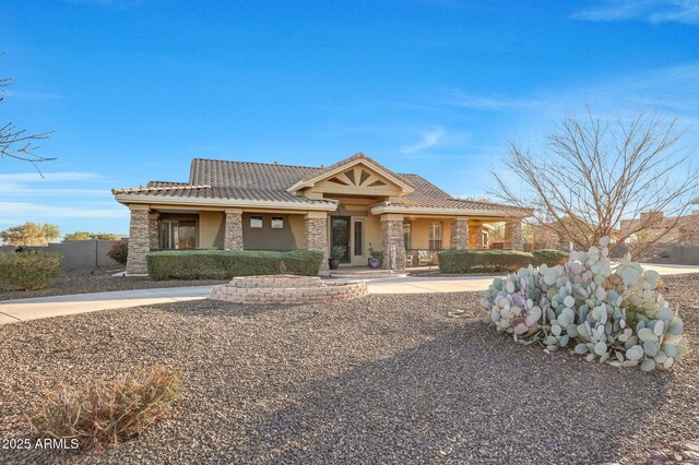 view of front of house with stone siding, fence, a tiled roof, and stucco siding