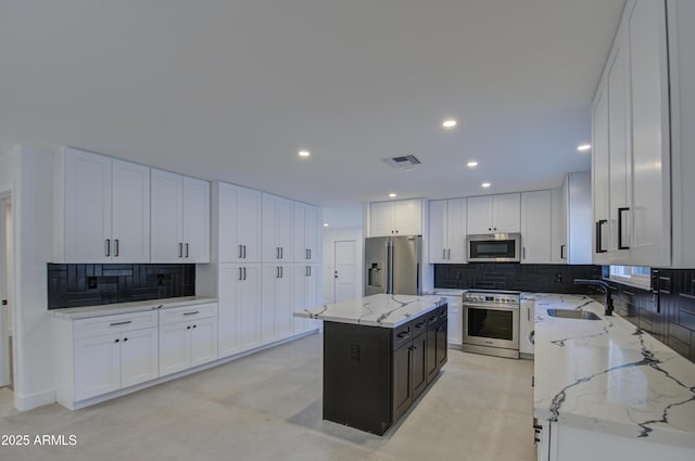 kitchen featuring sink, light stone counters, premium appliances, white cabinets, and a kitchen island