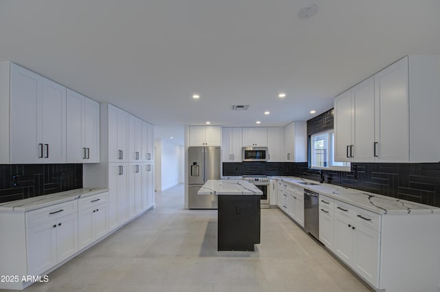 kitchen featuring white cabinetry, a center island, premium appliances, light stone countertops, and backsplash