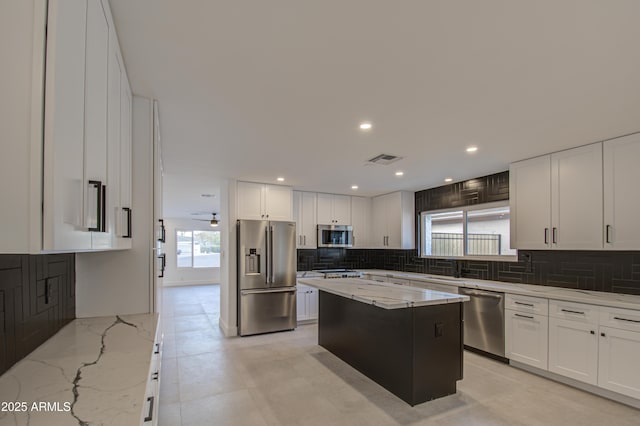 kitchen featuring white cabinetry, stainless steel appliances, light stone countertops, and a kitchen island