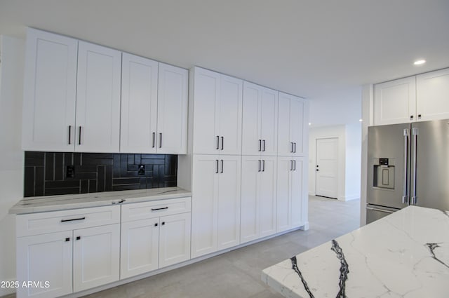 kitchen with light stone countertops, high quality fridge, white cabinets, and backsplash