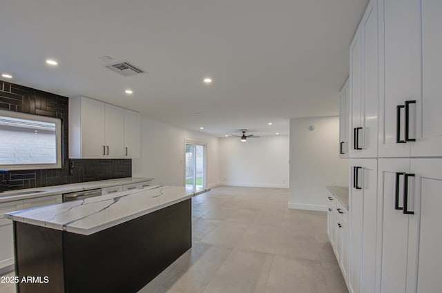 kitchen featuring a center island, stainless steel dishwasher, white cabinets, light stone countertops, and backsplash