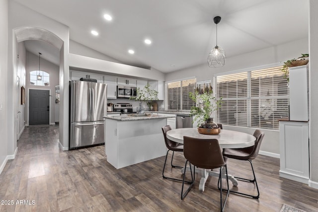 kitchen featuring pendant lighting, stainless steel appliances, white cabinets, a kitchen island, and vaulted ceiling