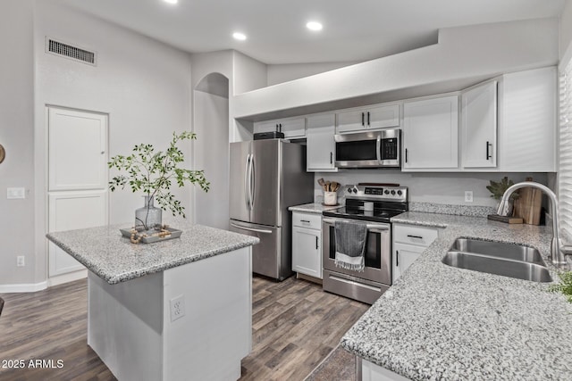 kitchen with sink, light stone counters, a center island, stainless steel appliances, and white cabinets