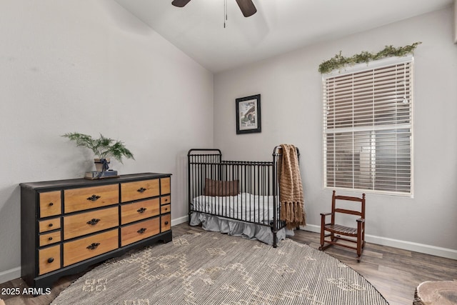 bedroom with dark hardwood / wood-style flooring, lofted ceiling, a nursery area, and ceiling fan