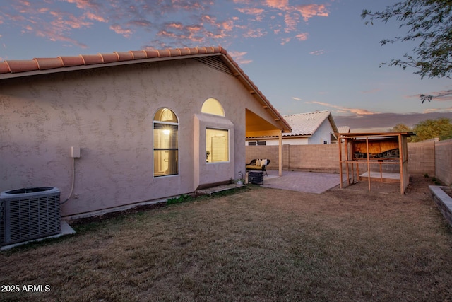 back house at dusk with central AC unit, a yard, and a patio area