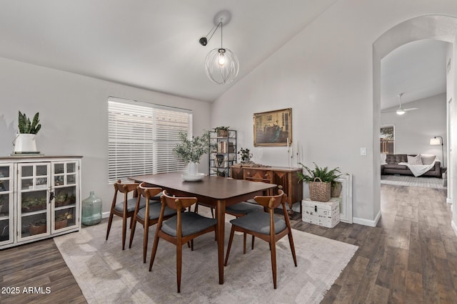 dining space featuring dark wood-type flooring, ceiling fan with notable chandelier, and high vaulted ceiling