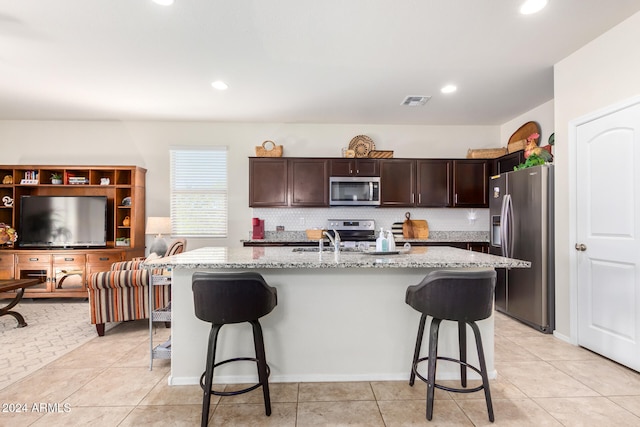 kitchen featuring a kitchen bar, backsplash, a kitchen island with sink, appliances with stainless steel finishes, and light stone counters