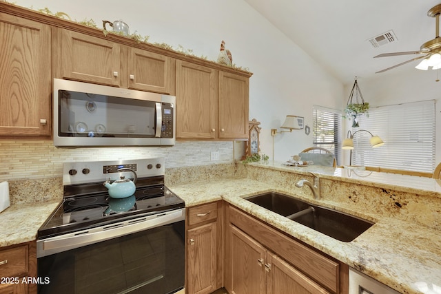 kitchen with appliances with stainless steel finishes, a sink, tasteful backsplash, a ceiling fan, and light stone counters
