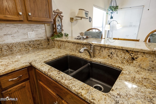kitchen with a sink, tasteful backsplash, light stone counters, and brown cabinets