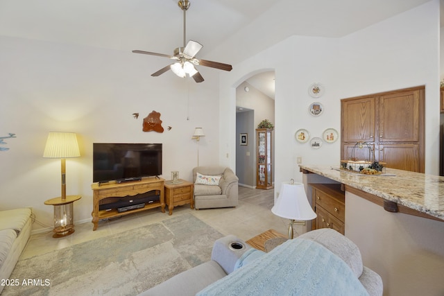 living area featuring light tile patterned floors, ceiling fan, arched walkways, baseboards, and high vaulted ceiling