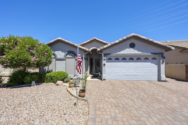 view of front of home with decorative driveway, an attached garage, a tiled roof, and stucco siding