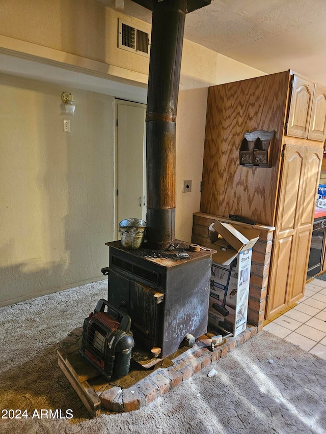 kitchen with a wood stove, a textured ceiling, light tile patterned flooring, and light brown cabinetry