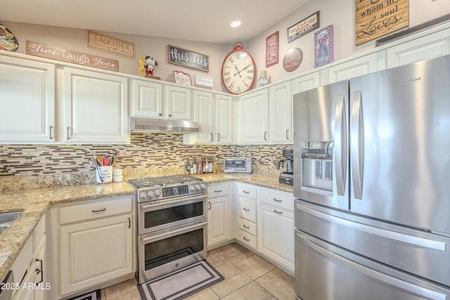 kitchen featuring light tile patterned flooring, under cabinet range hood, white cabinetry, appliances with stainless steel finishes, and tasteful backsplash