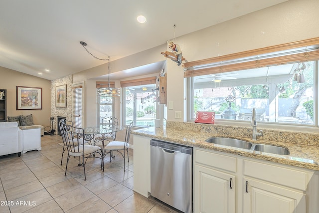 kitchen with lofted ceiling, stainless steel dishwasher, a sink, a stone fireplace, and ceiling fan
