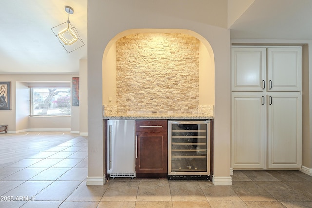 bar featuring light tile patterned flooring, beverage cooler, baseboards, decorative backsplash, and stainless steel fridge