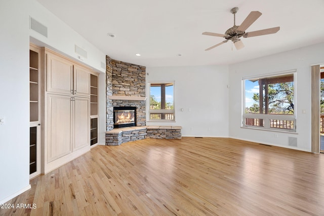 unfurnished living room with light wood-type flooring, a stone fireplace, and ceiling fan