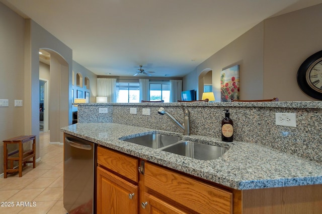 kitchen with light tile patterned floors, light stone countertops, brown cabinetry, dishwasher, and a sink