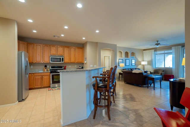 kitchen with arched walkways, open floor plan, appliances with stainless steel finishes, recessed lighting, and a breakfast bar area