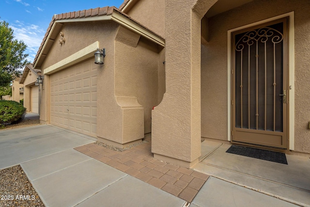 entrance to property featuring an attached garage, stucco siding, and a tile roof